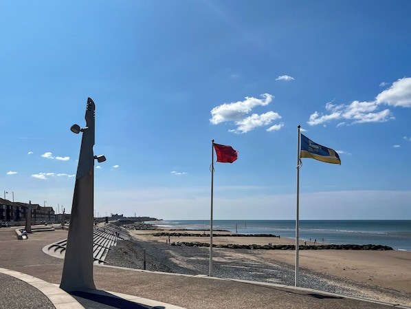 A beach with a flagpole, a sculpture, and a clear sky.
