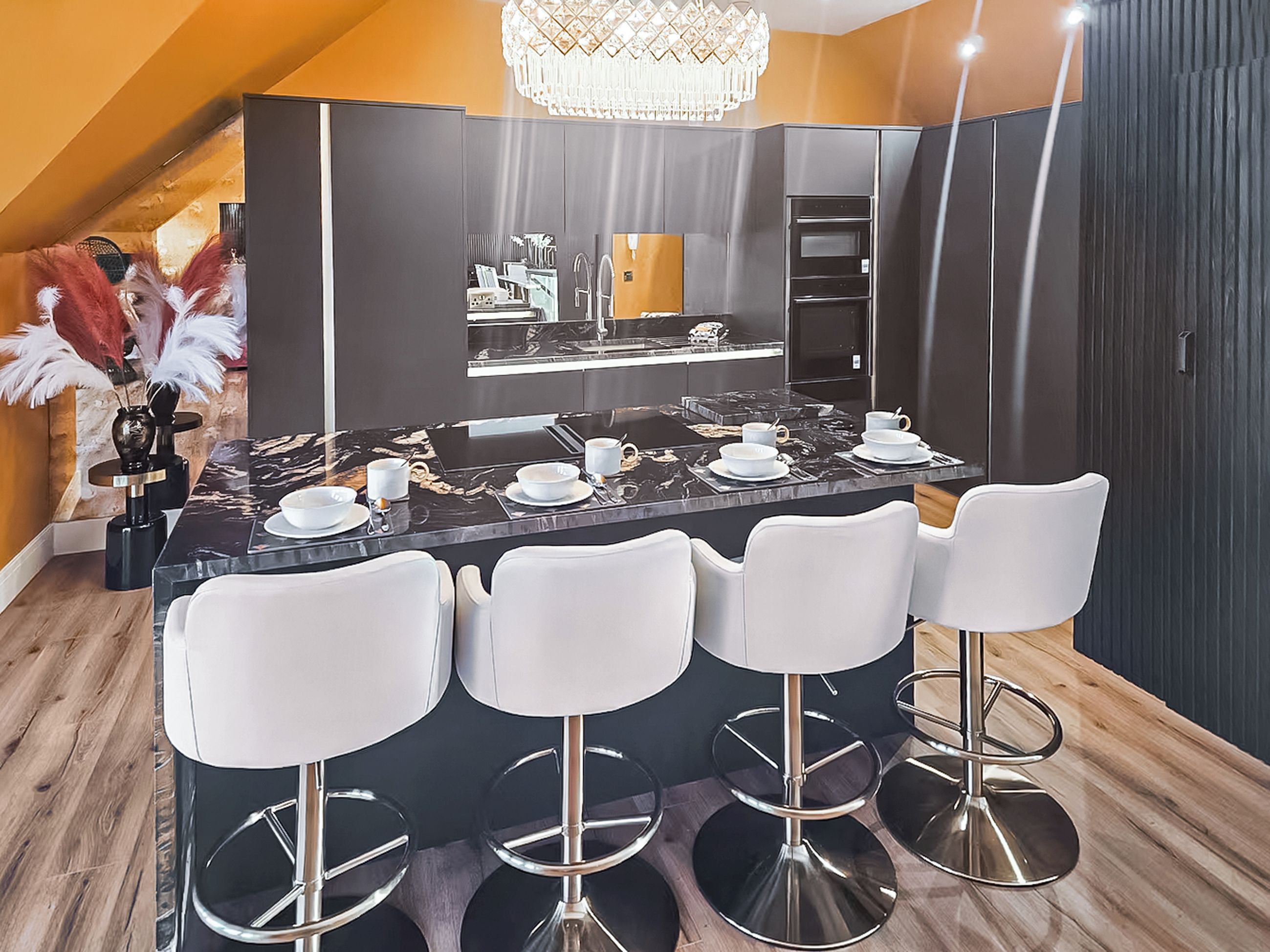 A modern kitchen with a central island, bar stools, and a chandelier.