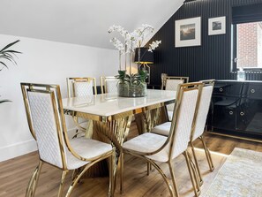 A dining area with a white marble table, gold chairs, and a vase of white flowers. - The Riverside Atelier (Durham)