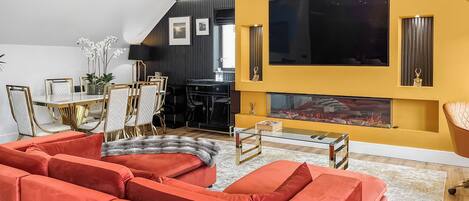 A modern living room with a fireplace, a large TV, and a dining area with a table and chairs.