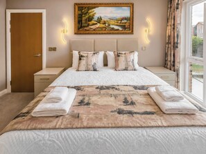 A hotel room with a large bed, a painting on the wall, and a view through the window. - The Riverside Atelier (Durham)