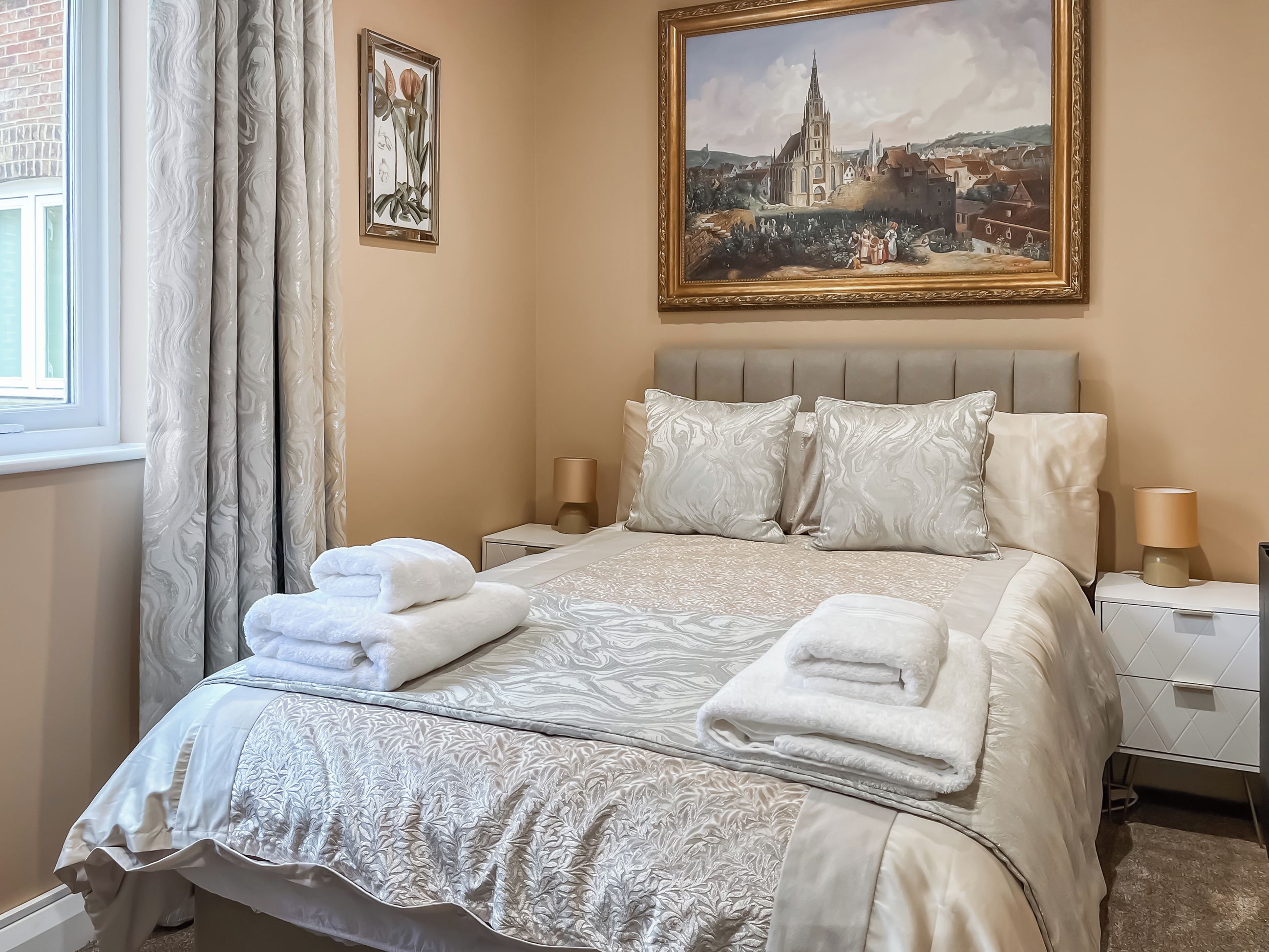 A hotel room with a large bed, two bedside tables, a painting on the wall, and a window with curtains.
