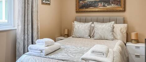 A hotel room with a large bed, two bedside tables, a painting on the wall, and a window with curtains.