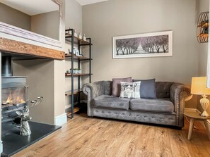 A living room with a fireplace, a gray sofa with decorative pillows, a wooden floor, and a framed painting on the wall. - Lock Keeper's Cottage (Dutton Locks, near Northwich)