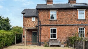 A two-story brick house with a front door, a bench, and a small garden area. - Lock Keeper's Cottage (Dutton Locks, near Northwich)