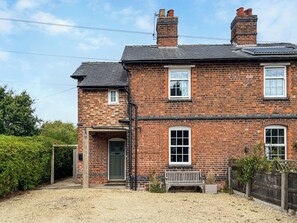 A two-story brick house with a front door, a bench, and a small garden area.