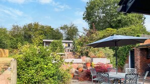 An outdoor patio area with a table and chairs, surrounded by greenery and a brick wall. - Lock Keeper's Cottage (Dutton Locks, near Northwich)
