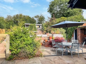 An outdoor patio area with a table and chairs, surrounded by greenery and a brick wall.