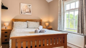 A bedroom with a wooden bed, two bedside lamps, a radiator, and a window with curtains. - Lock Keeper's Cottage (Dutton Locks, near Northwich)