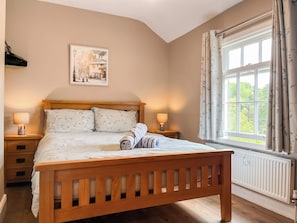A bedroom with a wooden bed, two bedside lamps, a radiator, and a window with curtains.