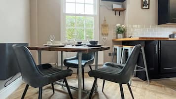 A modern kitchen with a dining table set for four, two black chairs, and a window with a view of greenery.