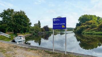Un canal con un cartel que indica Dutton Locks, una embarcación amarrada a la izquierda y una zona ajardinada con un banco.