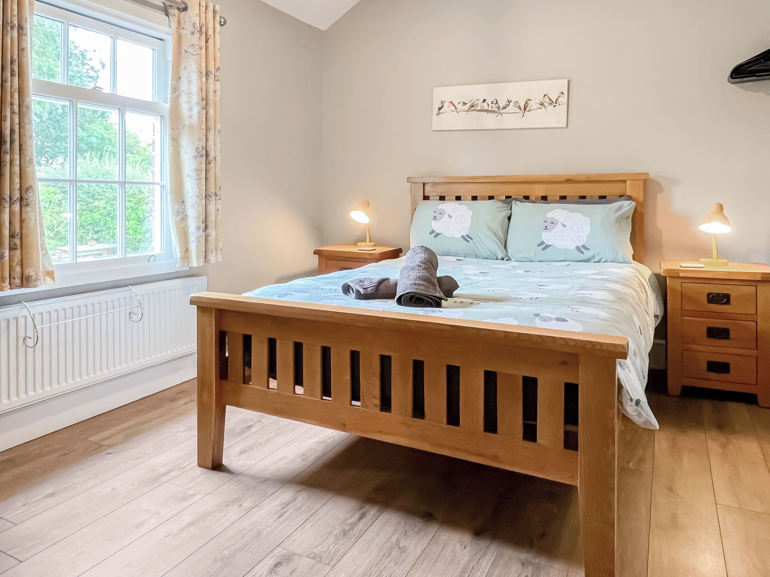 Un dormitorio con una cama de madera, un radiador, una ventana con cortinas y una obra de arte colgada en la pared.