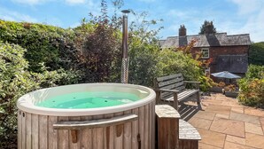 A wooden hot tub with a clear water surface, a wooden bench, and a patio area with stone tiles. - Lock Keeper's Cottage (Dutton Locks, near Northwich)