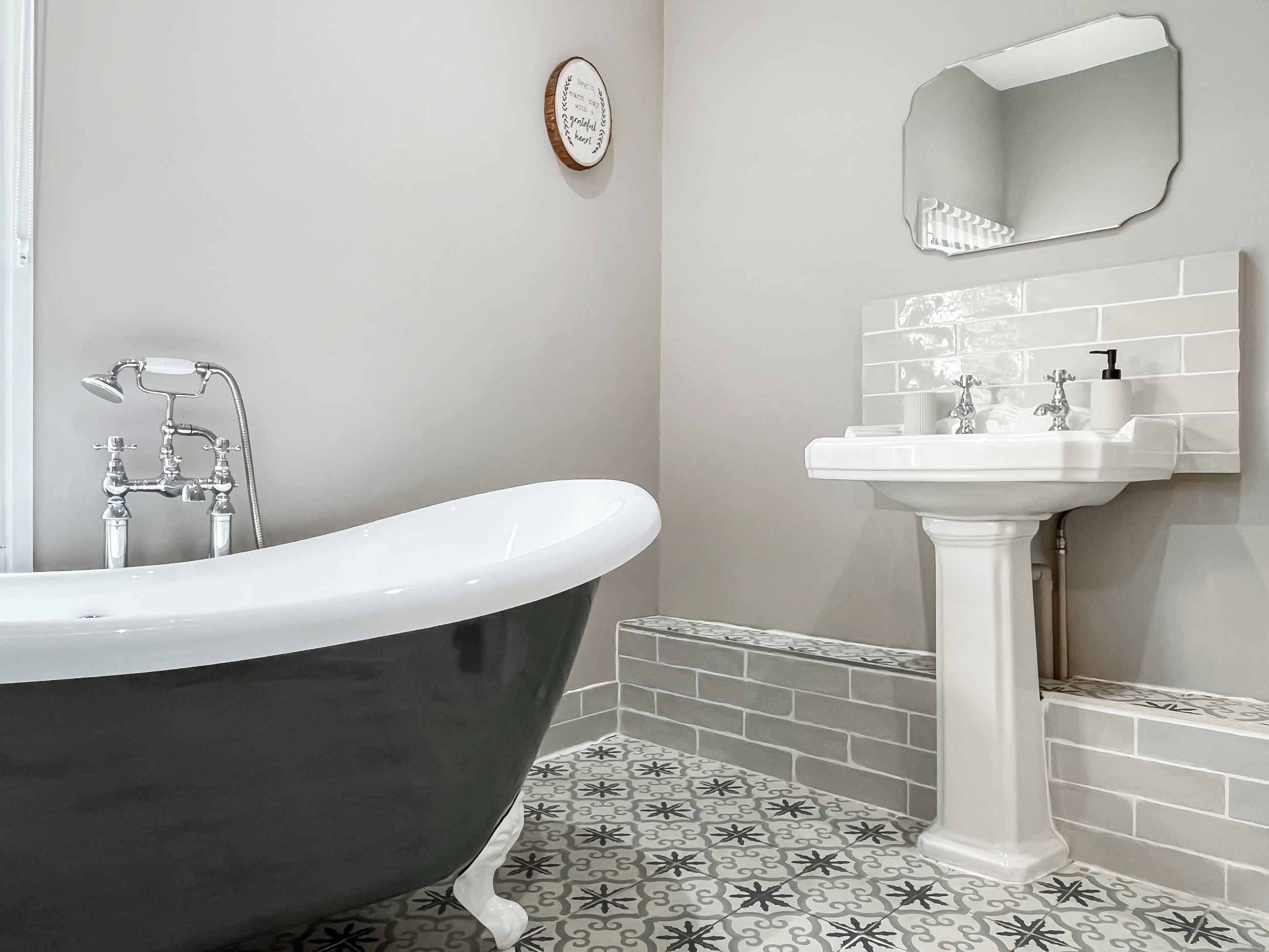 Une salle de bain avec une baignoire sur pieds, un lavabo sur colonne et des carreaux de sol à motifs.