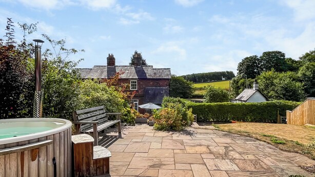 A patio area with a hot tub, wooden bench, and stone flooring. - Lock Keeper's Cottage (Dutton Locks, near Northwich)