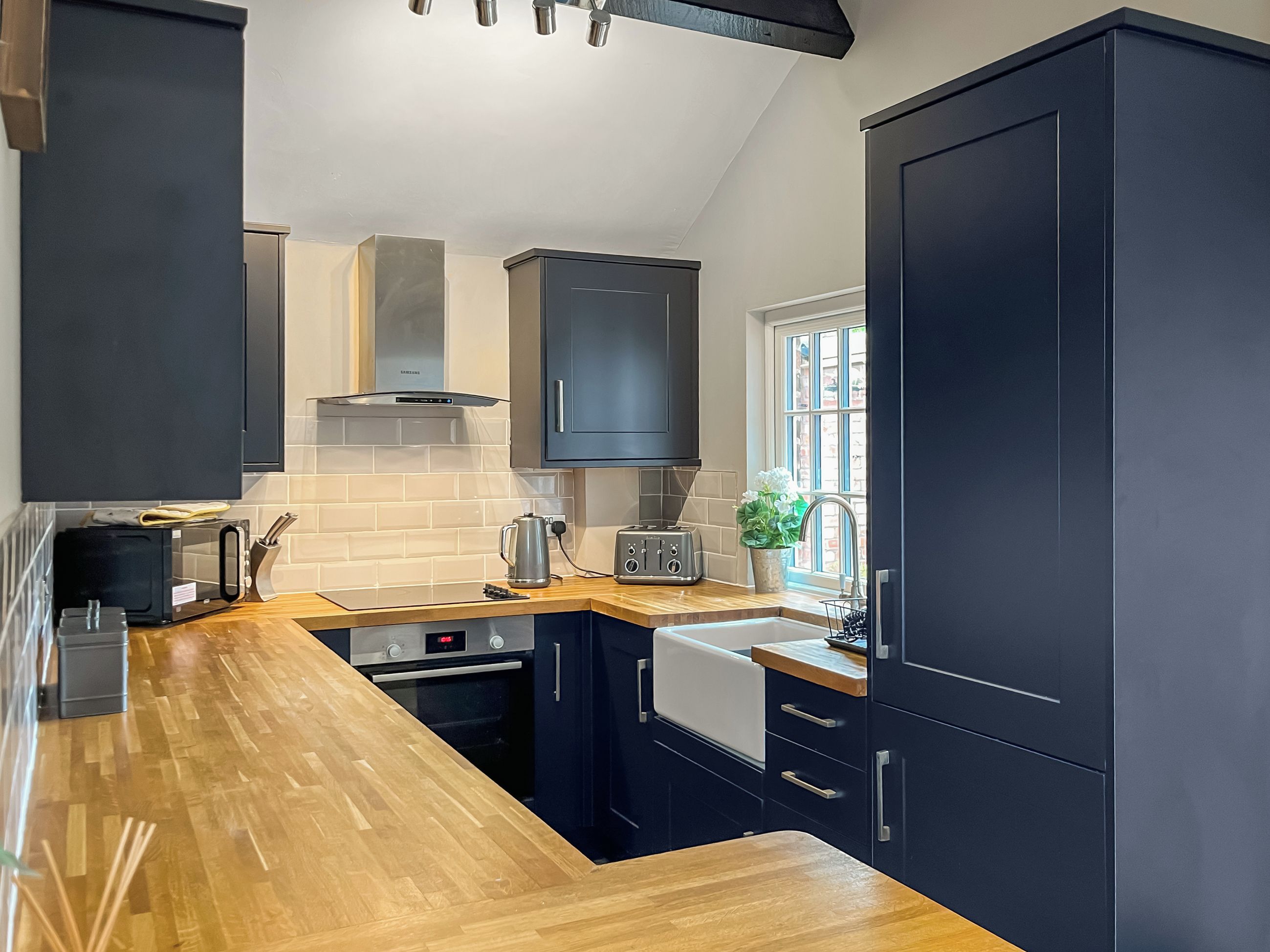 A modern kitchen with dark cabinetry, a wooden countertop, a built-in oven, a microwave, and a toaster.