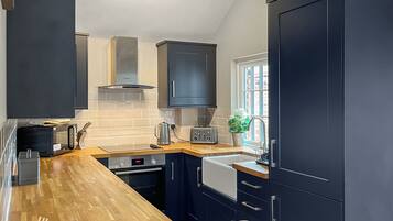 A modern kitchen with dark cabinetry, a wooden countertop, a built-in oven, a microwave, and a toaster.