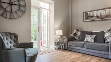 A living room with a sofa, a chair, a clock, a lamp, and a painting on the wall.