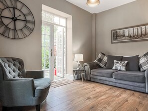 A living room with a sofa, a chair, a clock, a lamp, and a painting on the wall. - Lock Keeper's Cottage (Dutton Locks, near Northwich)