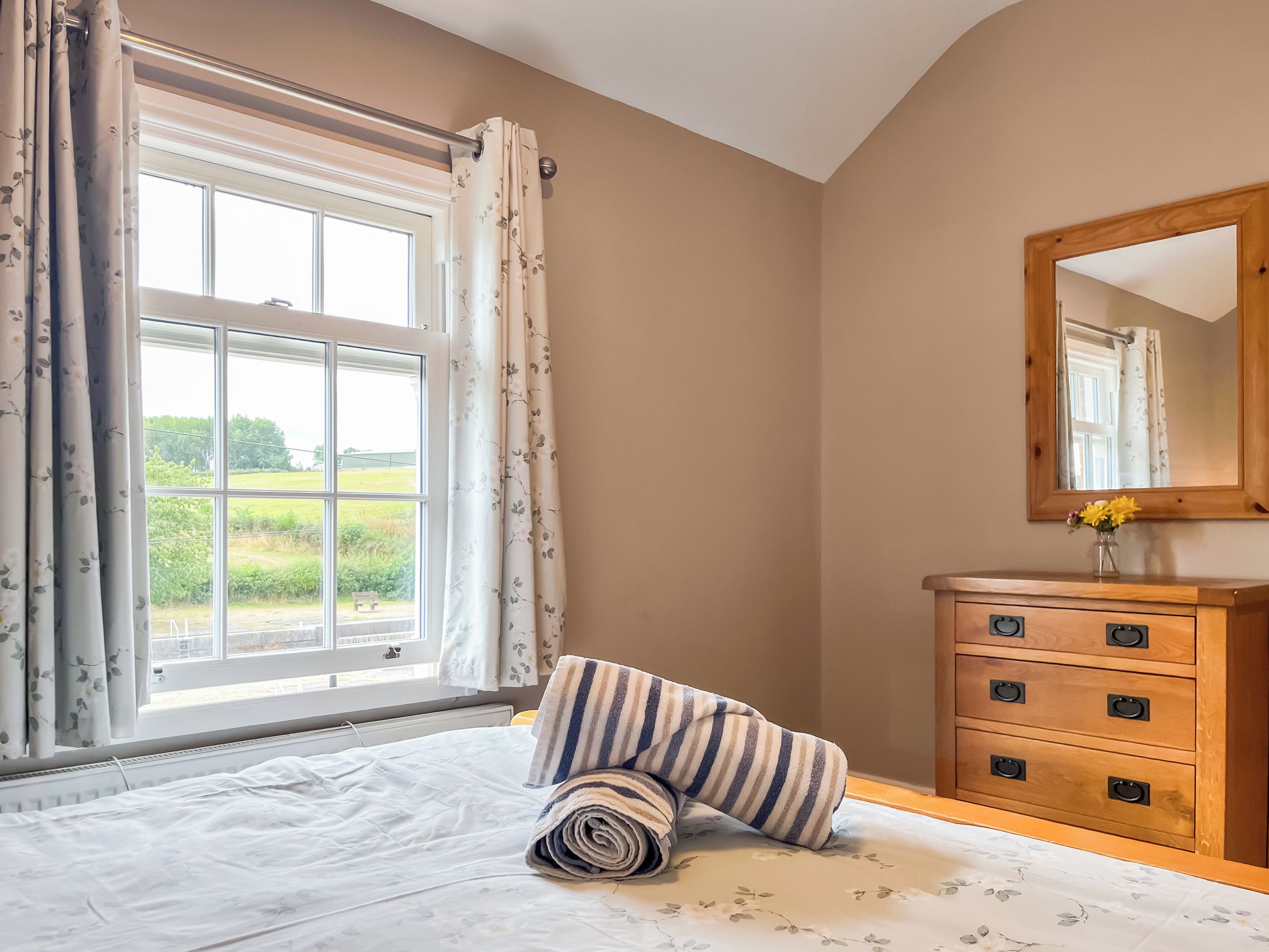 A bedroom with a large window, a wooden dresser with drawers, and a bed with a floral bedspread.