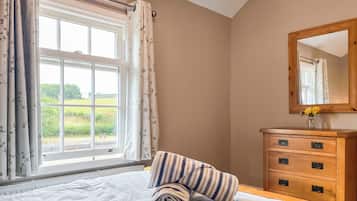 A bedroom with a large window, a wooden dresser with drawers, and a bed with a floral bedspread.