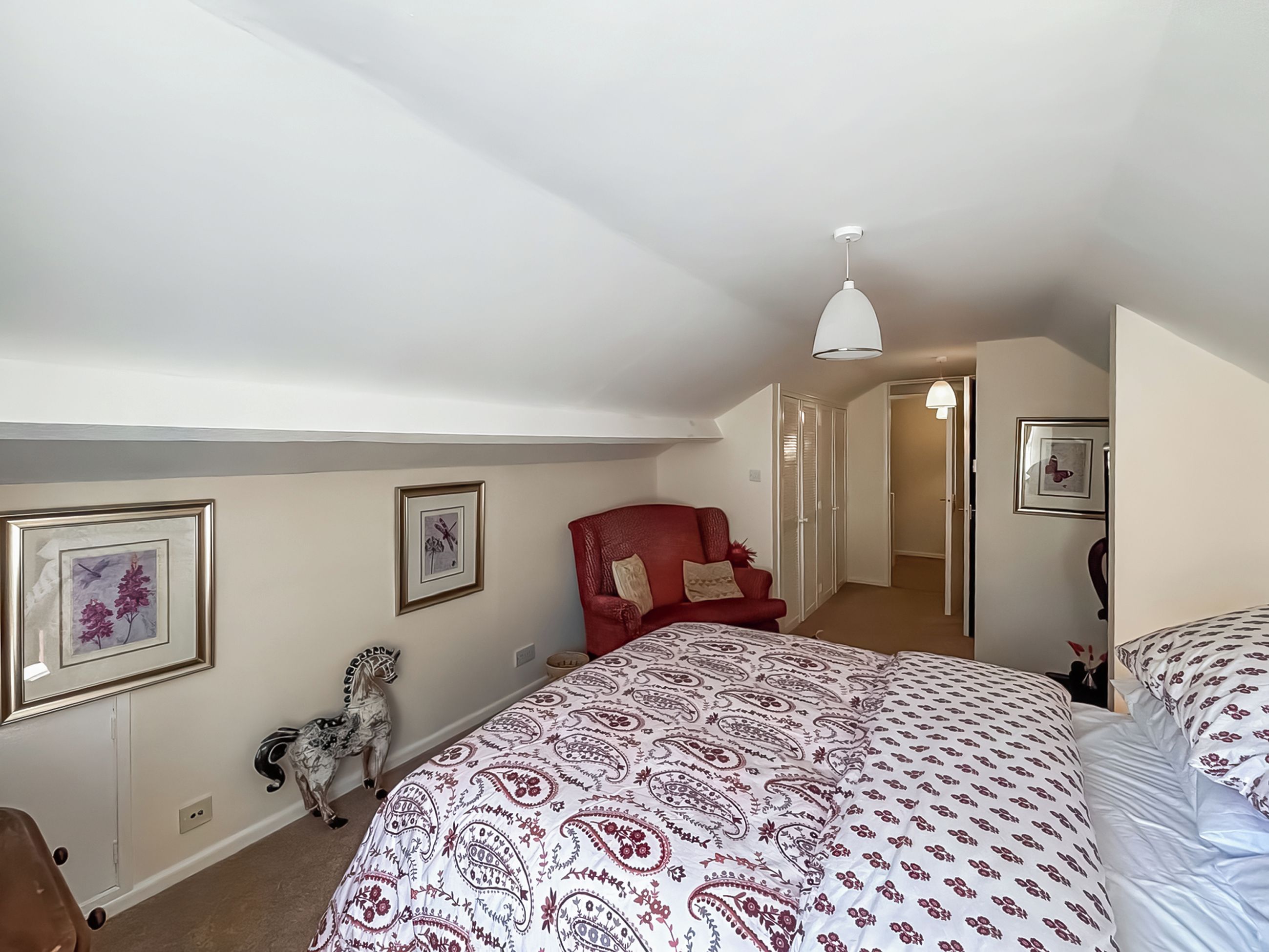 Ein Schlafzimmer mit einem großen Bett, einem roten Sessel, einer weißen Decke und einer Tür zu einem anderen Raum.