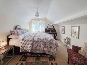 Een slaapkamer met een bed, nachtkastje, kaptafel, spiegel, ingelijste foto's en een decoratief paardbeeldje.