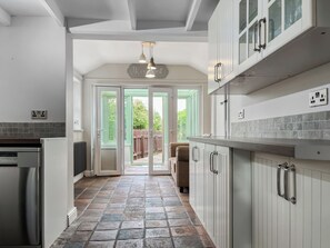 A kitchen with a stone floor, white cabinets, and a view through glass doors to an outdoor area. - 2 bedroom accommodation in Acton Bridge, near Northwich (Acton Bridge, near Northwich)