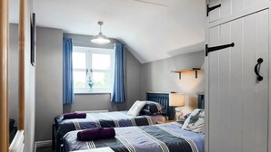 Una camera da letto con due letti, una finestra con tende, una ventola a soffitto e un comodino.