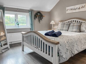 A bedroom with a bed, a radiator, a window with curtains, a bedside table with a lamp, and a wall-mounted plant. - 2 bedroom accommodation in Acton Bridge, near Northwich (Acton Bridge, near Northwich)