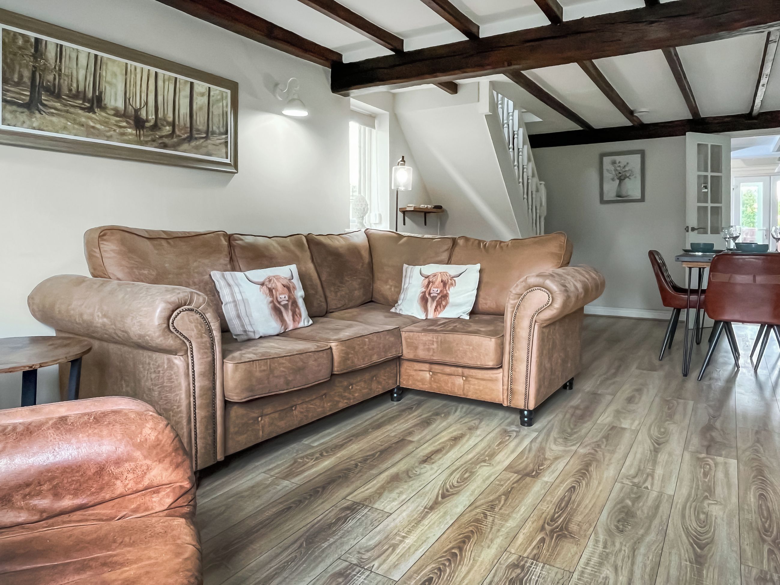 A spacious living area with a brown leather sofa, two decorative pillows, a wooden floor, and a dining area in the background.