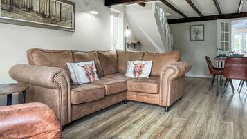 A spacious living area with a brown leather sofa, two decorative pillows, a wooden floor, and a dining area in the background.
