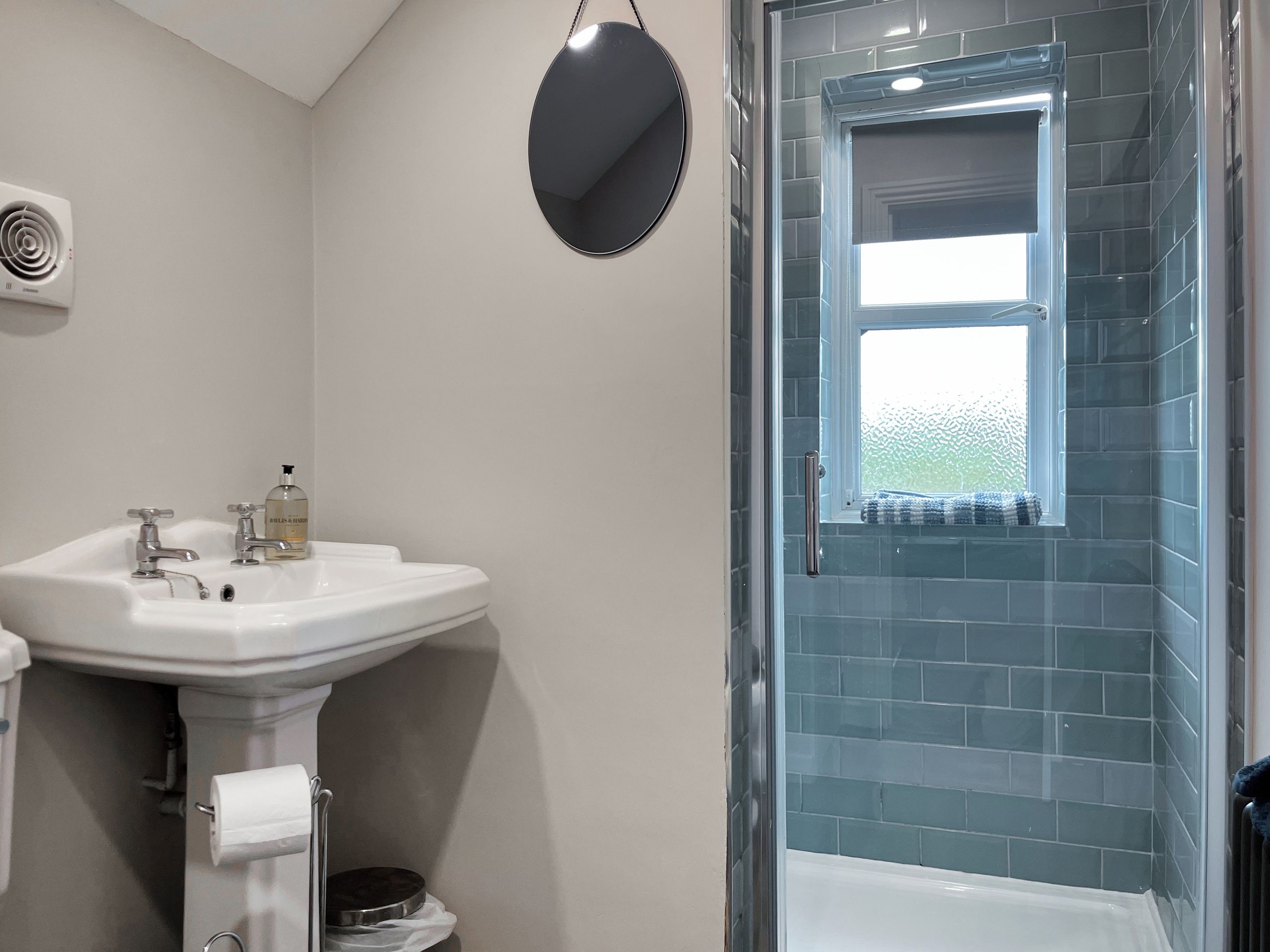 Une salle de bain avec un lavabo blanc, un miroir, une fenêtre et un espace douche.