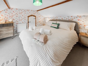 A bedroom with a large bed, a wooden dresser, a radiator, and a mirror on the wall. - 4 bedroom accommodation in Old Dalby (Old Dalby)
