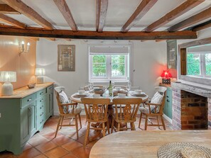 A dining area with a wooden table set for four, surrounded by chairs, a green cabinet, and a fireplace. - 4 bedroom accommodation in Old Dalby (Old Dalby)
