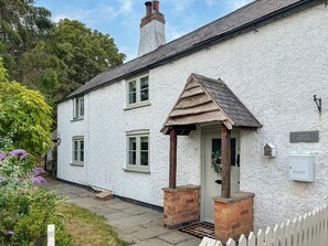 Ein weißes Cottage mit einer Holzveranda, einem Schornstein und einem Briefkasten mit der Aufschrift 'POST'.