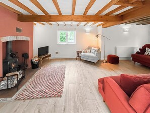A living room with a fireplace, a sofa, a red ottoman, and a television. - 4 bedroom accommodation in Old Dalby (Old Dalby)