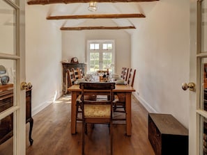 Ein Esszimmer mit einem Holztisch, gedeckt für vier Personen, flankiert von Holzstühlen, einem Fenster mit Aussicht und einem Holzschrank.