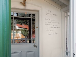 A white door with a window, a wall with a welcome message, and a green door frame. - 4 bedroom accommodation in Horsham Saint Faith (Horsham Saint Faith)
