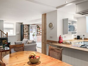 A modern kitchen with a wooden island, a dining area with a wooden table and chairs, and a view into the adjacent living space. - The Old School House (Kirkbymoorside)