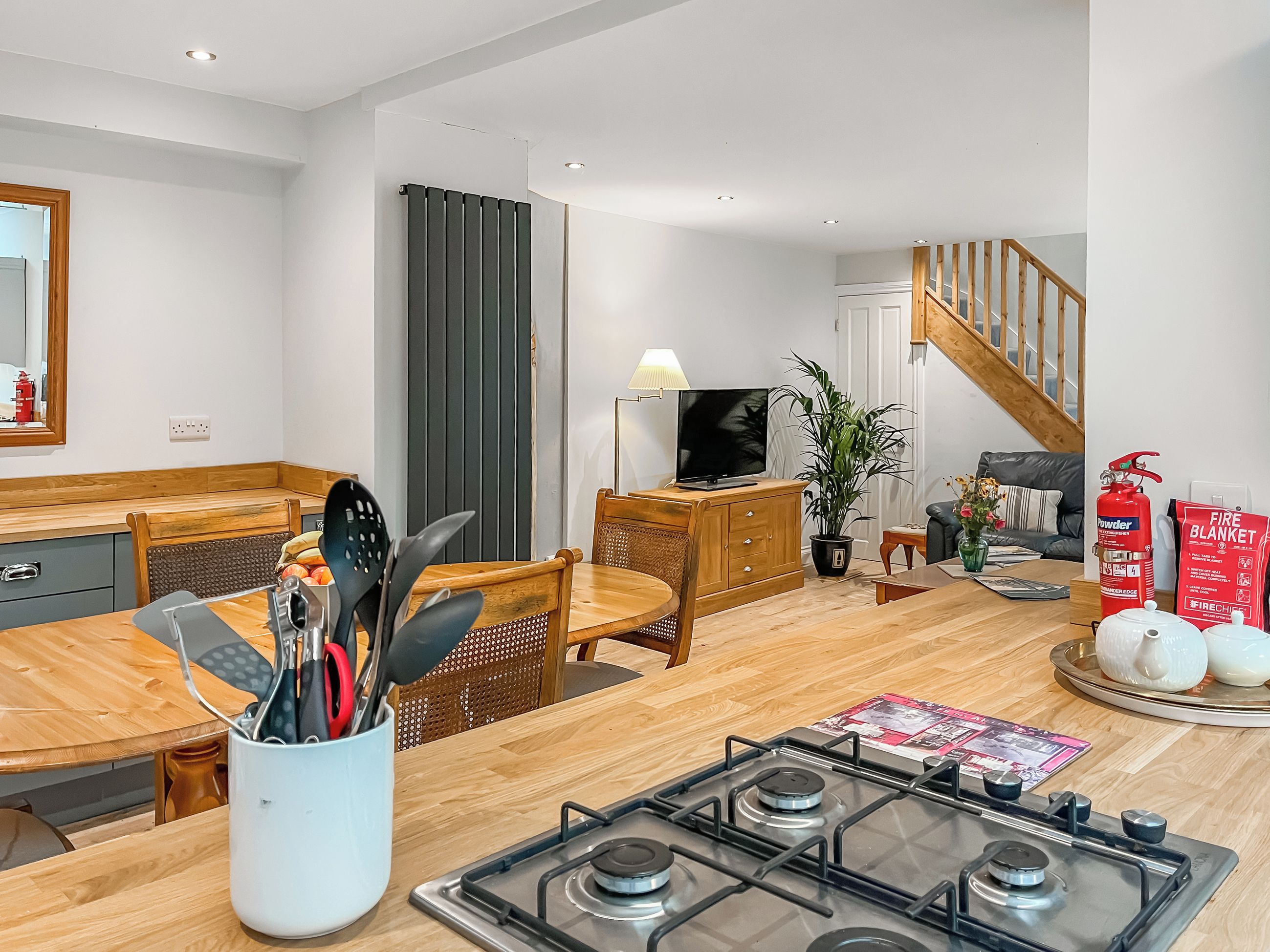 A modern kitchen with a gas stove, wooden furniture, a dining table, and a staircase leading to an upper level.