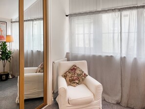 Ett rum med en vit soffa, en prydnadskudde med blommönster, ett element och randiga gardiner.