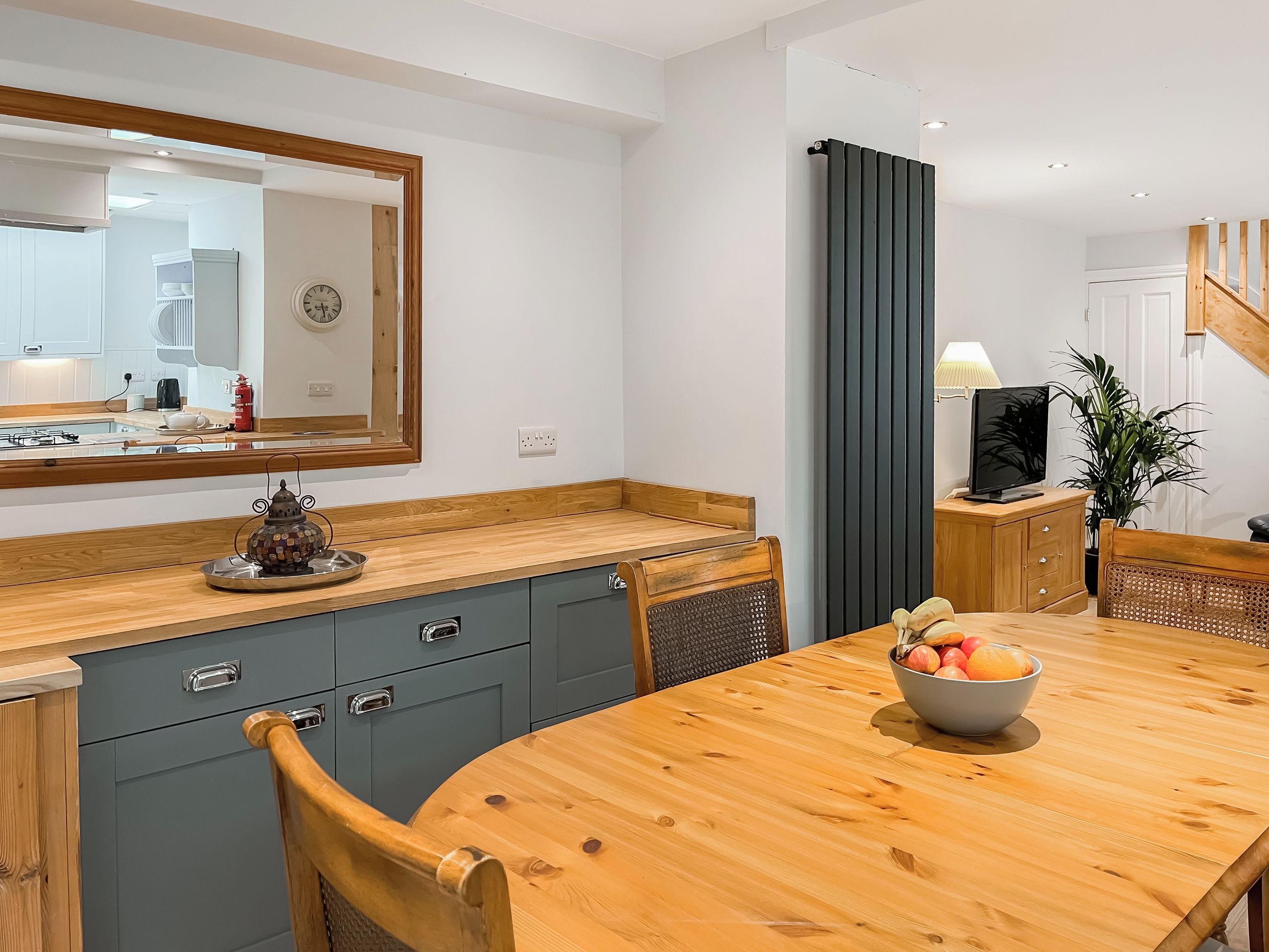A modern kitchen with a wooden table, grey cabinets, and a mirror above the counter.