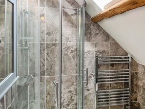A shower with a glass door, a metal towel rack, and a tiled wall with a wooden beam. - The Old School House (Kirkbymoorside)