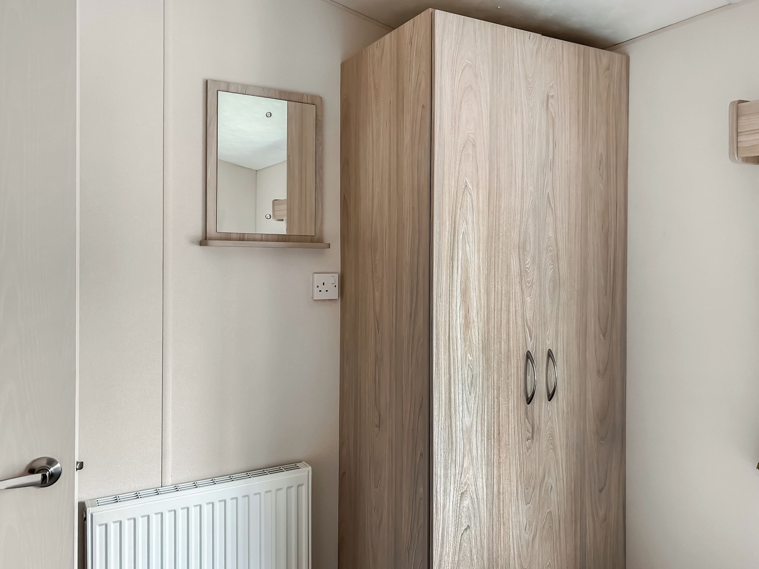 A room with a wardrobe, a mirror, a radiator, and a door.