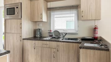 Cocina compacta con armarios de madera, microondas, hervidor de agua, lavabo y extintor.