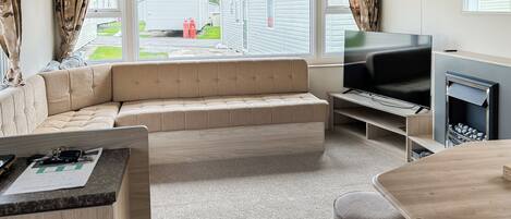A modern living room with a sofa, TV, fireplace, and a view of mobile homes outside.
