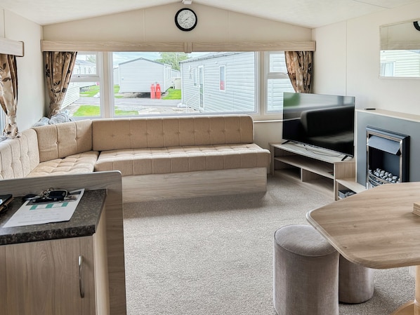 Een moderne woonkamer met een bank, televisie, open haard en uitzicht op stacaravans.