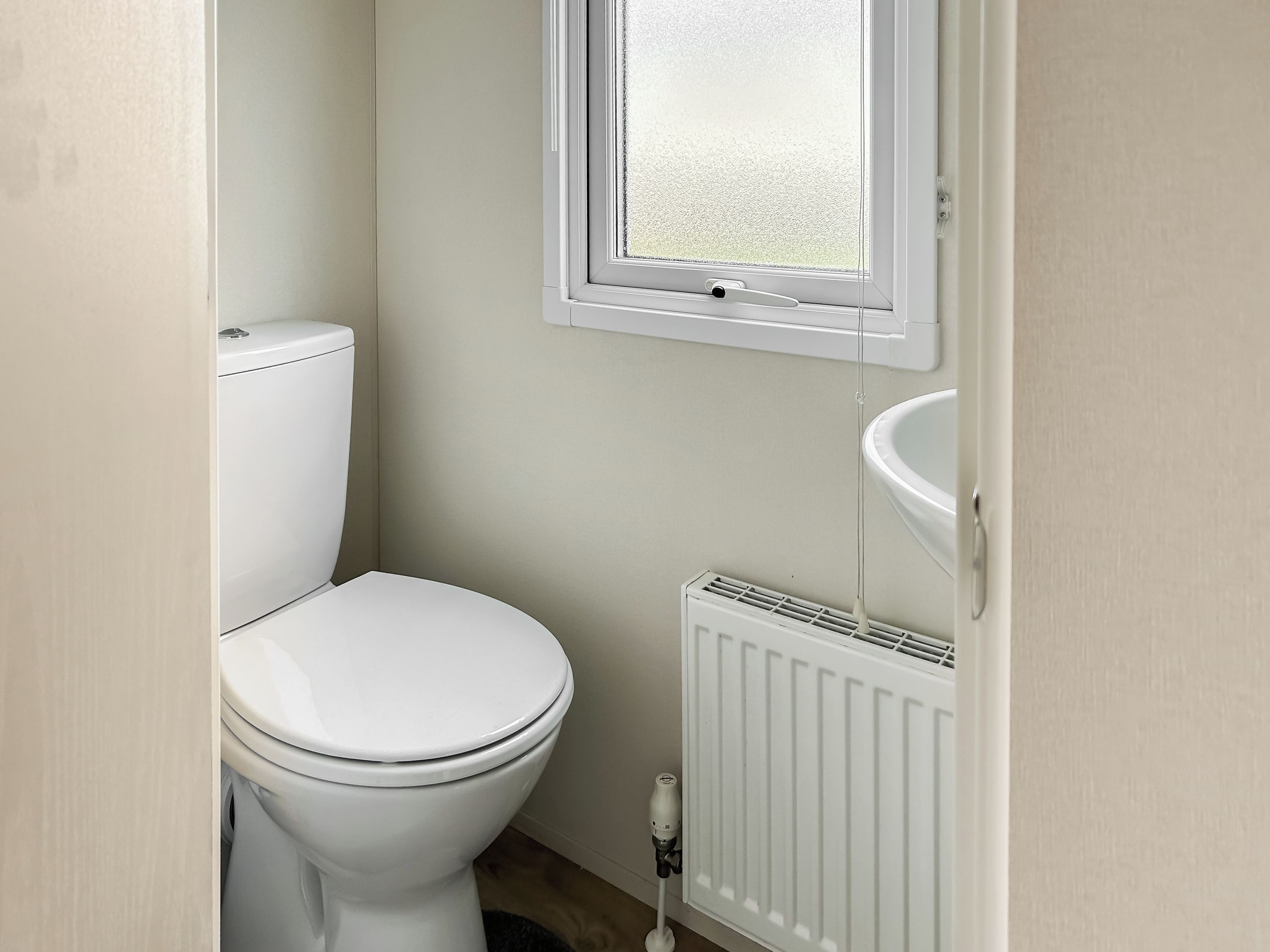 Ein kleines, sauberes Badezimmer mit Toilette, Fenster und Heizkörper.